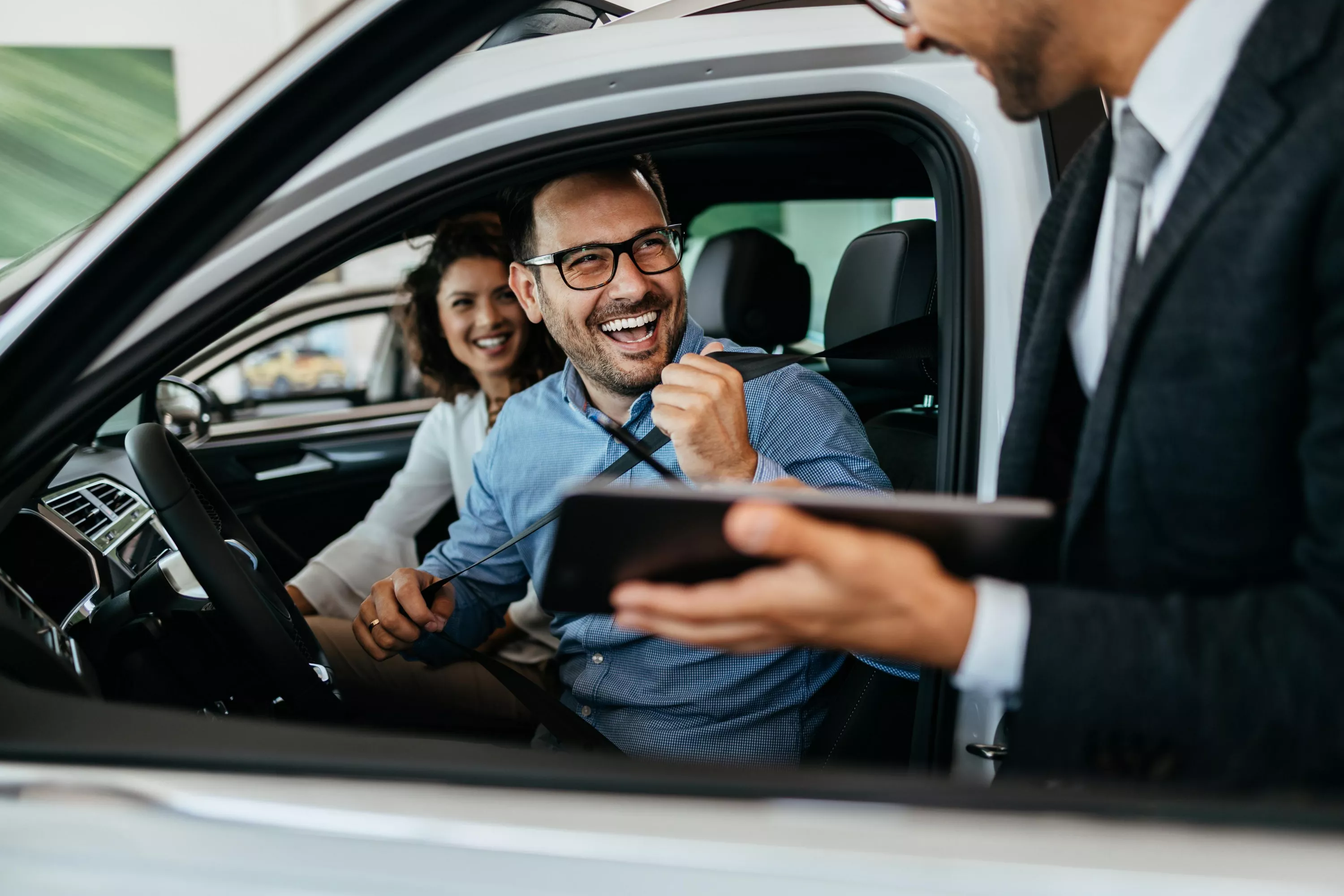 Ein Mann mit Tablet steht am Fenster eines Autos, in dem lachende Personen sitzen.