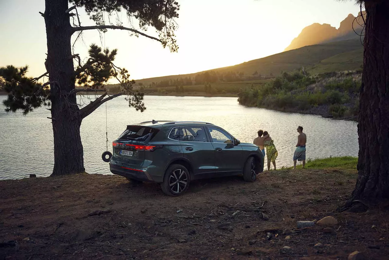 Drei Personen stehen an einem VW Tiguan vor einem See bei Sonnenuntergang in den Bergen