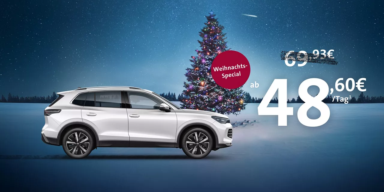 silberner- vw-tiguan-steht-vor-weihnachtlicher-landschaft-mit-bunt-beleuchtetem-tannenbaum