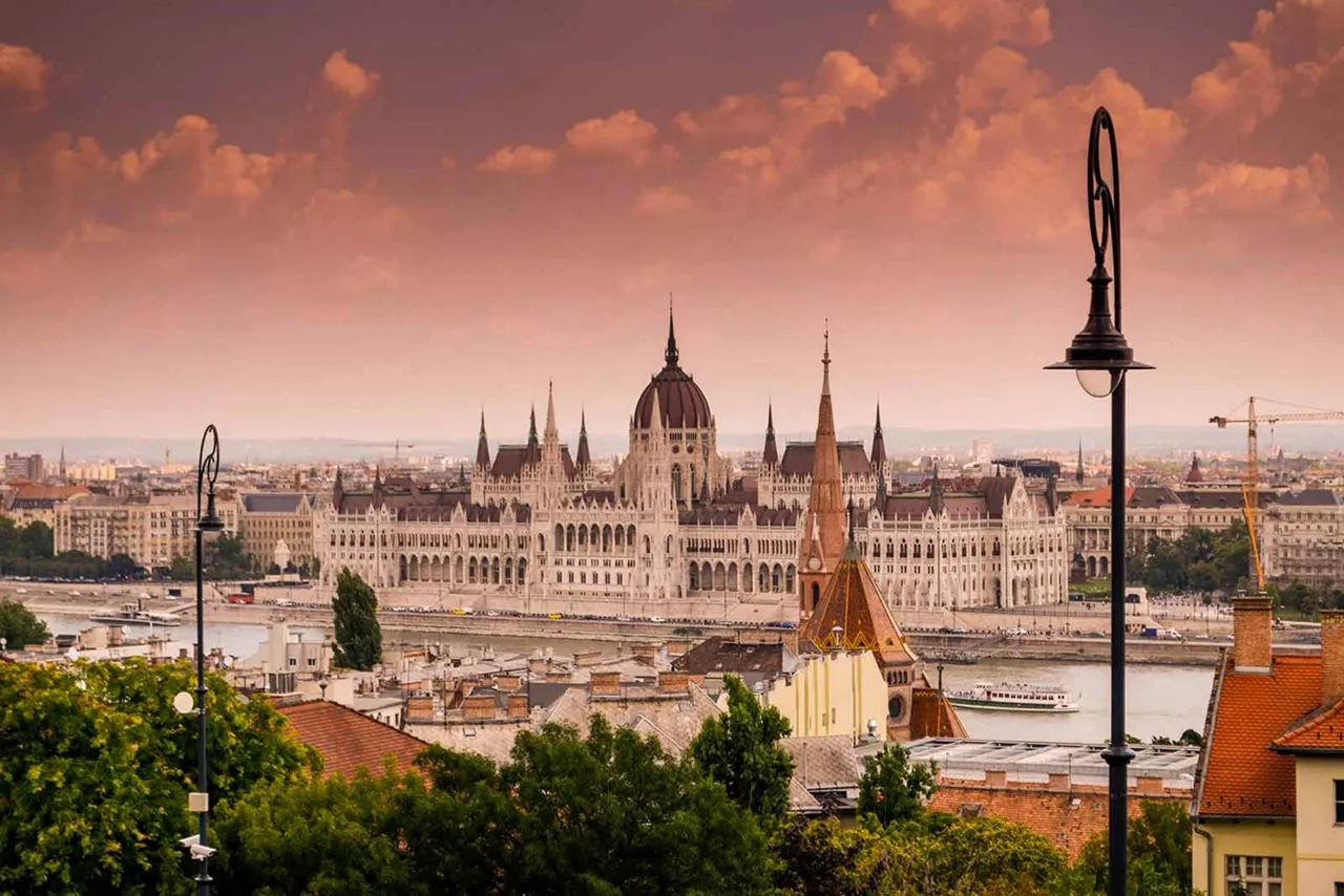 Blick auf das ungarische Parlamentsgebäude in Budapest mit Donau, historischer Altstadt und warmem Abendhimmel