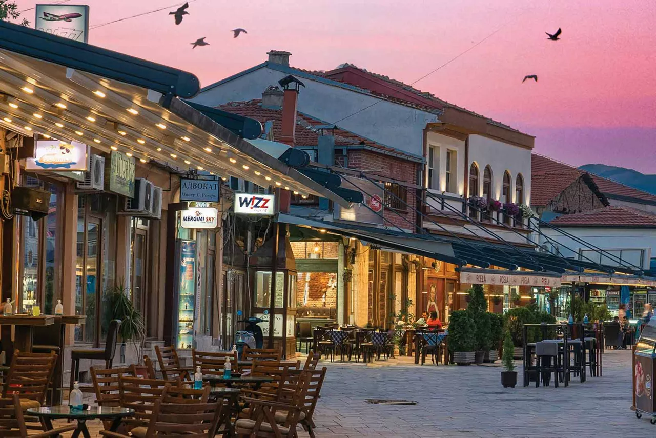 Abendliche Fußgängerzone mit Restaurants, beleuchteten Terrassen, Tischen im Freien und historischen Gebäuden bei Sonnenuntergang in Nordmazedonien