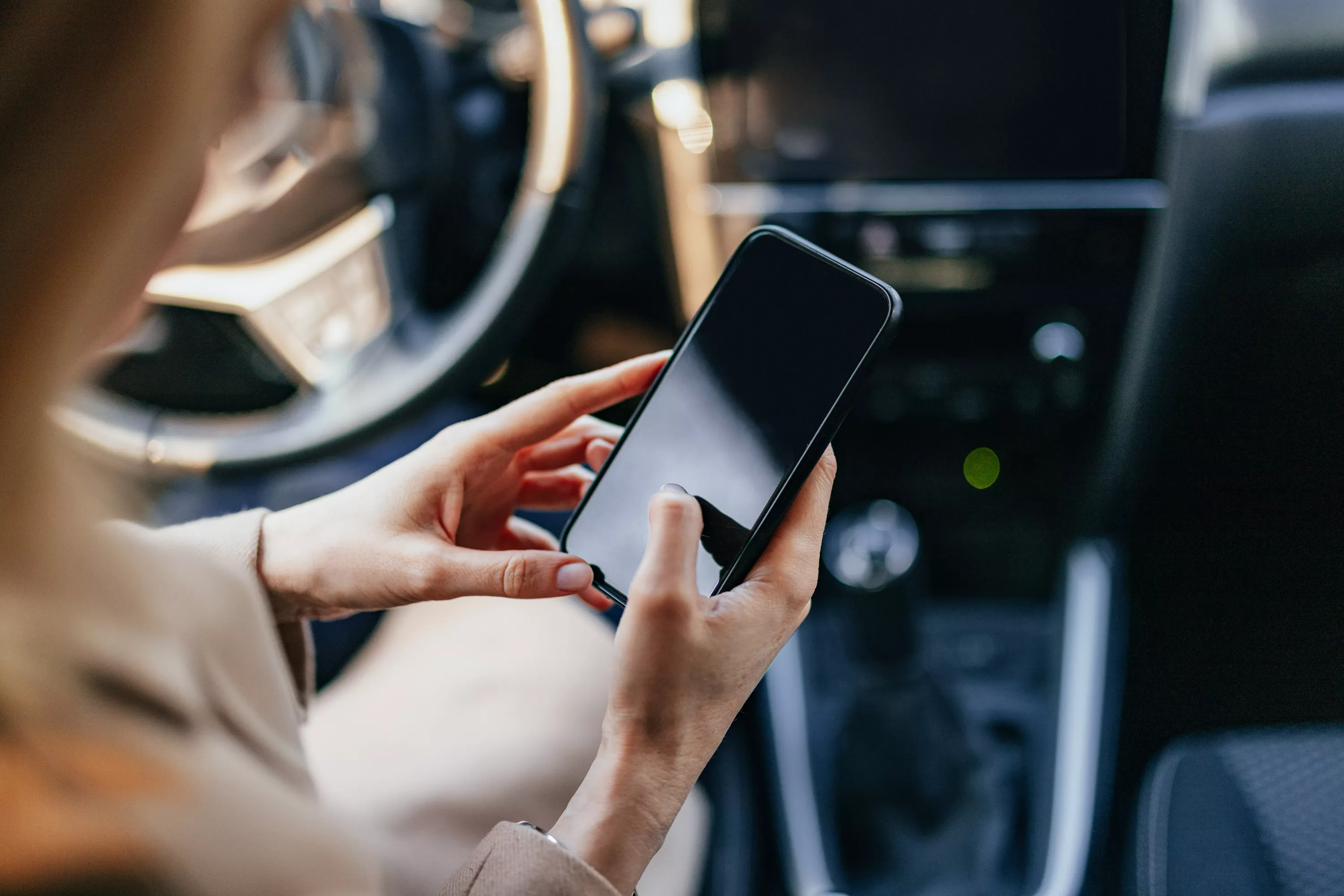 Frau sitzt am Steuer eines Pkw und tippt etwas in ihr Smartphone.