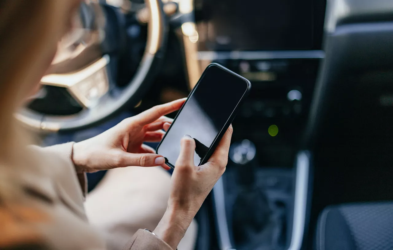 Frau sitzt am Steuer eines Pkw und tippt etwas in ihr Smartphone.
