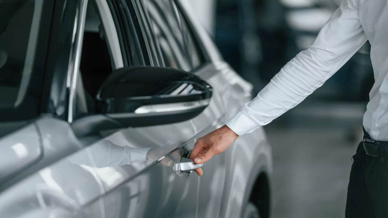 Nahaufnahme der Hand eines Mannes, der einen Reisepass, eine Landkarte und anderen Unterlagen in der Hand hält. Mit der gleichen Hand greift er nach einem Koffer. 