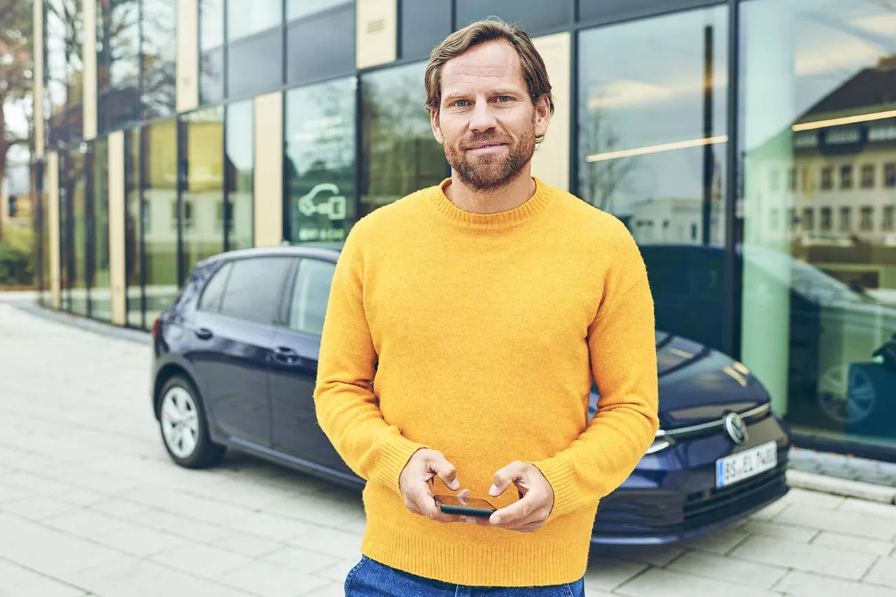 lächelnde-person-im-gelben-pulli-vor-auto-und-vermietstation-von-vw-fs-rent-a-car