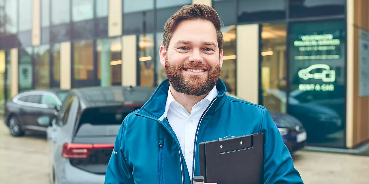 lächelnder-vermietrepräsentant-der-autovermietung-vw-fs-rent-a-car-vor-vermietstation