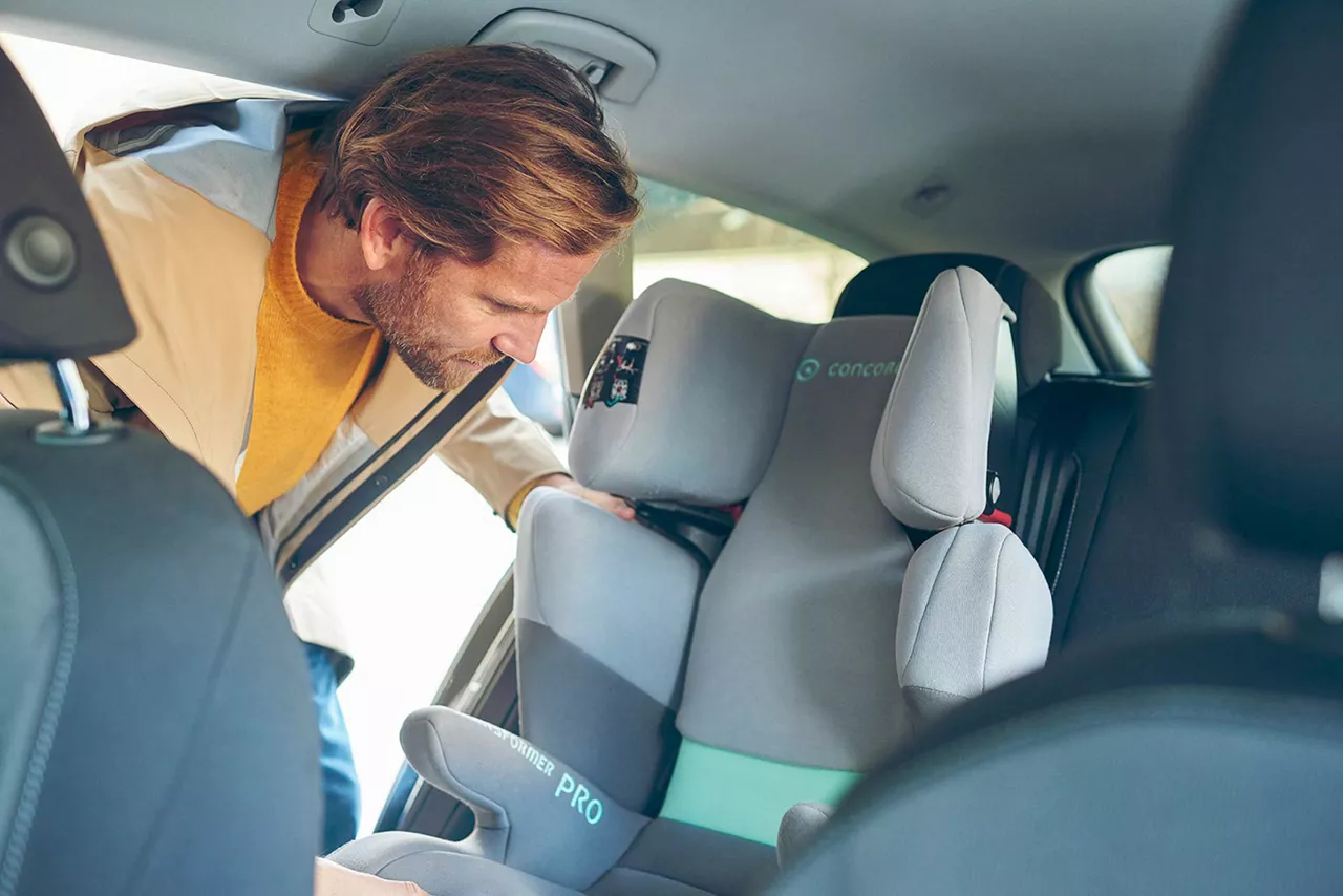 Ein Vater befestigt eine Kindersitzerhöhung mit Rückenlehne im Auto – sorgfältige Vorbereitung für sicheres Mitfahren.