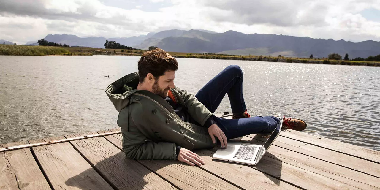 Mann eröffnet mit dem Laptop auf einem Steg den Plus Sparbrief.