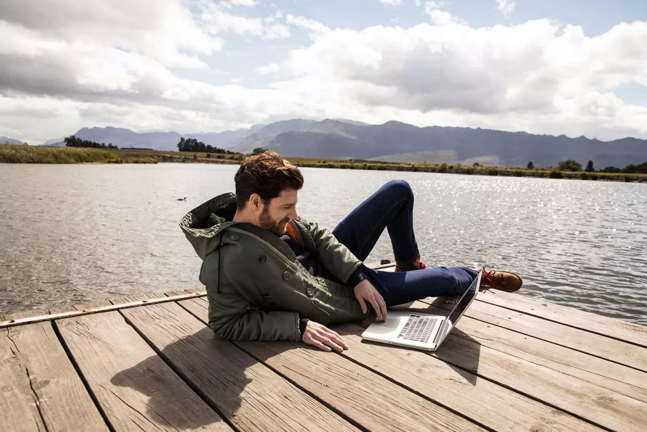 Mann eröffnet mit dem Laptop auf einem Steg den Plus Sparbrief.