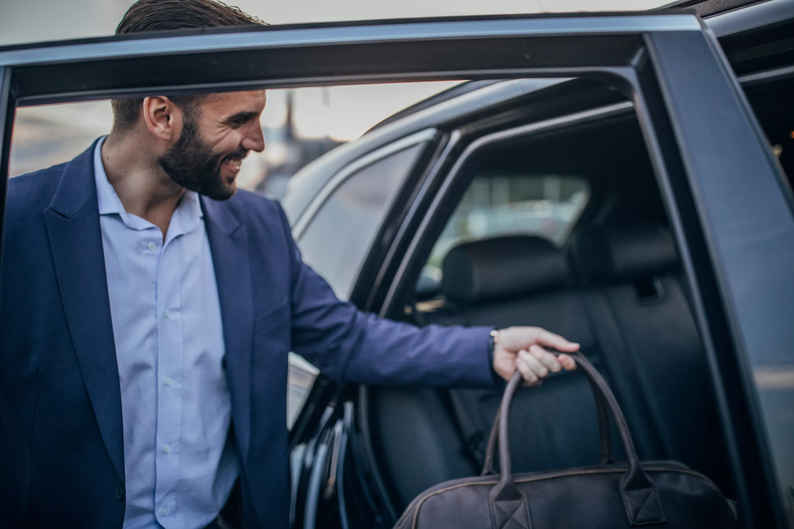 Mann in Anzug und mit Tasche in der Hand steigt in ein Fahrzeug ein.