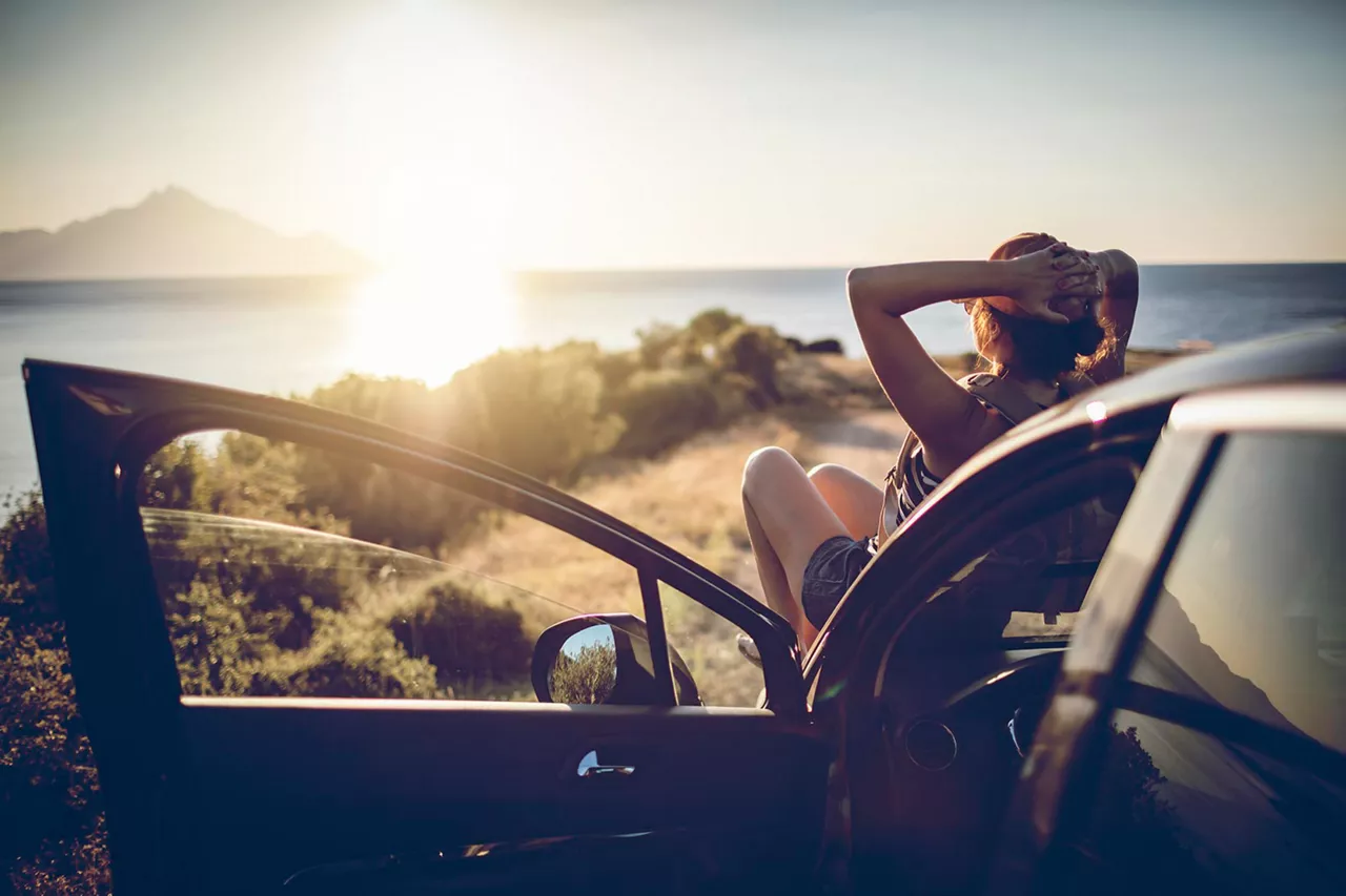 frau-sitzt-auf-motorhaube-eines-autos-und-genießt-sonnenuntergang-über-meer