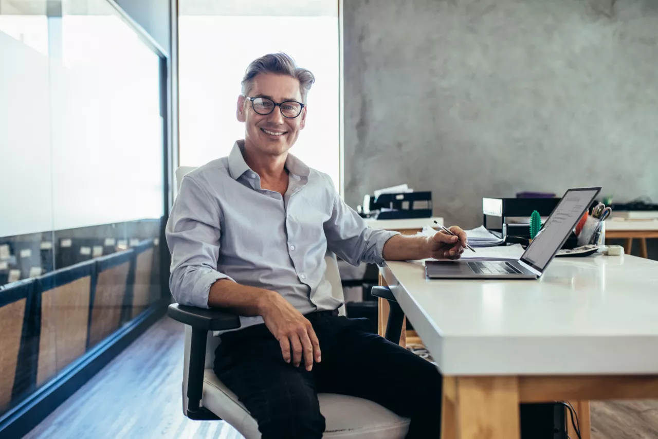 Ein Geschäftsmann sitzt in seinem Büro an seinem Schreibtisch und freut sich über sein Kapitalkonto Business.