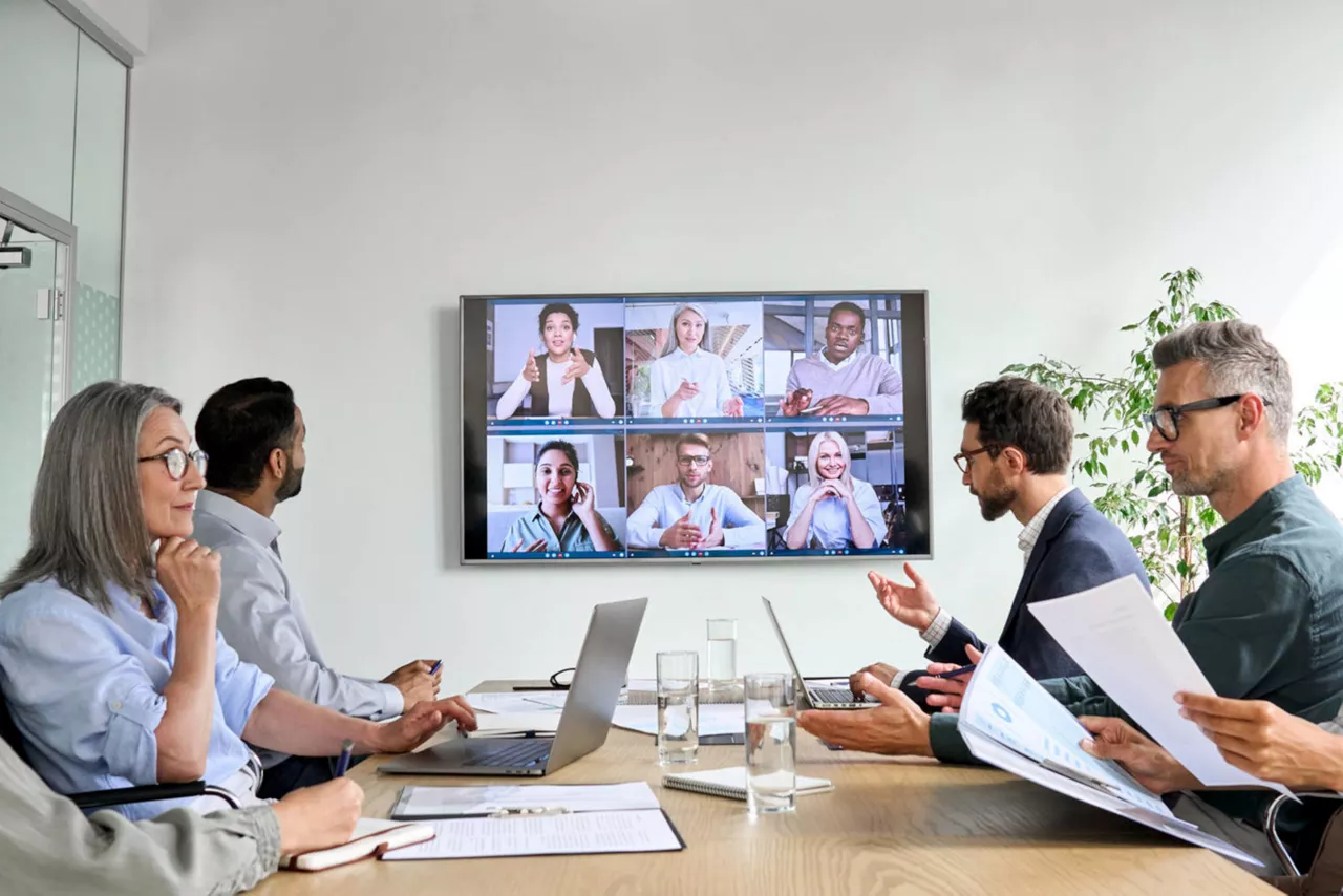 Mitarbeiter an einem Konferenztisch mit Videoübertragung