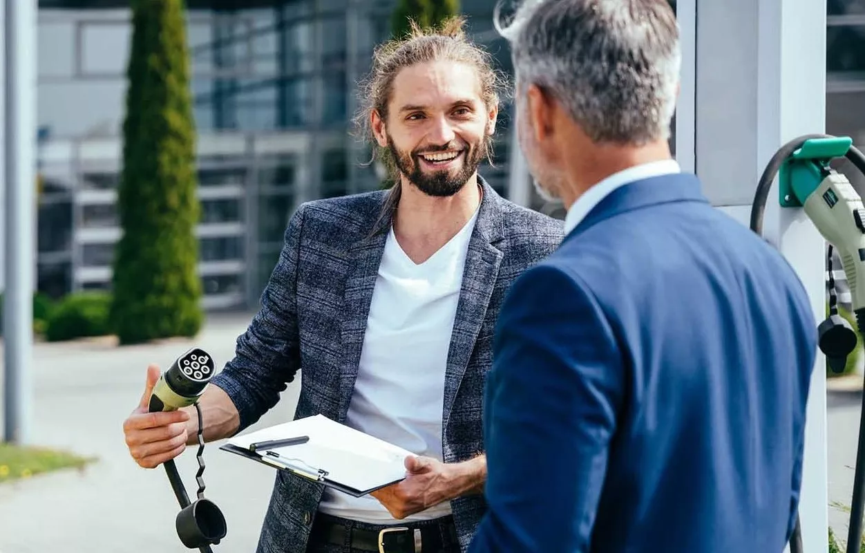 Fuhrparkmanager die draußen vor einer Ladesäule stehen und sich unterhalten.