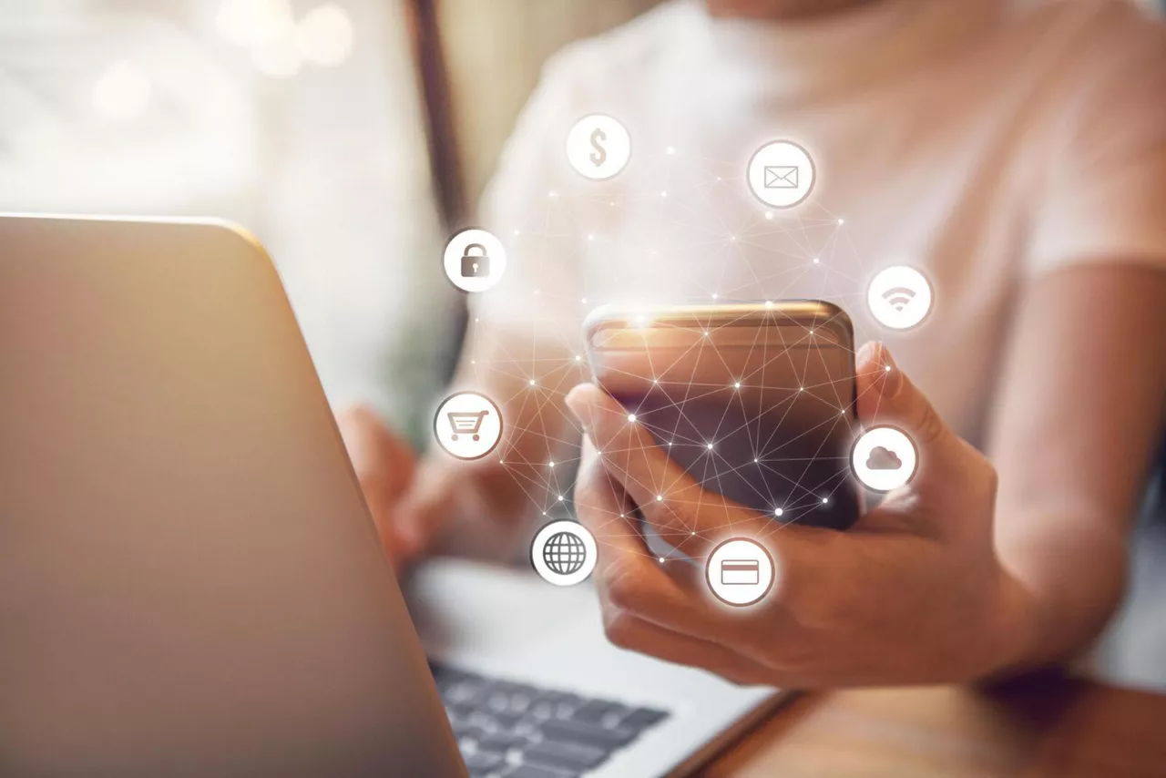 Person hält ein Smartphone mit leuchtenden, grafischen Elementen in der Hand, während sie am Laptop sitzt.