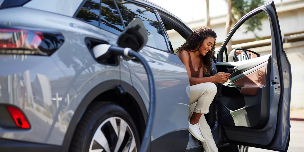 Una mujer mirando el móvil sentada en el asiento del copiloto con la puerta del coche abierta.