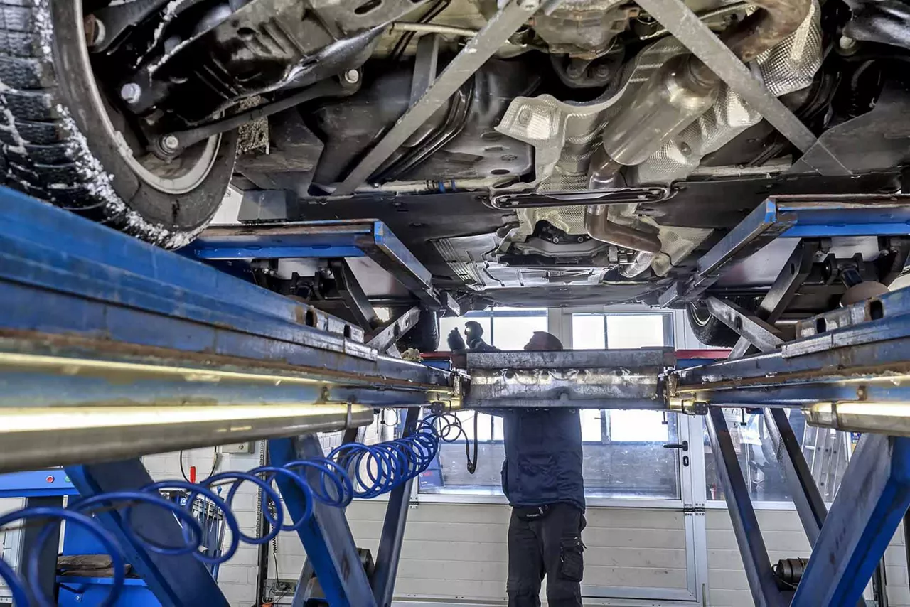 Mechaniker arbeitet in einer Werkstatt an einem Auto, das auf einer Hebebühne angehoben ist.