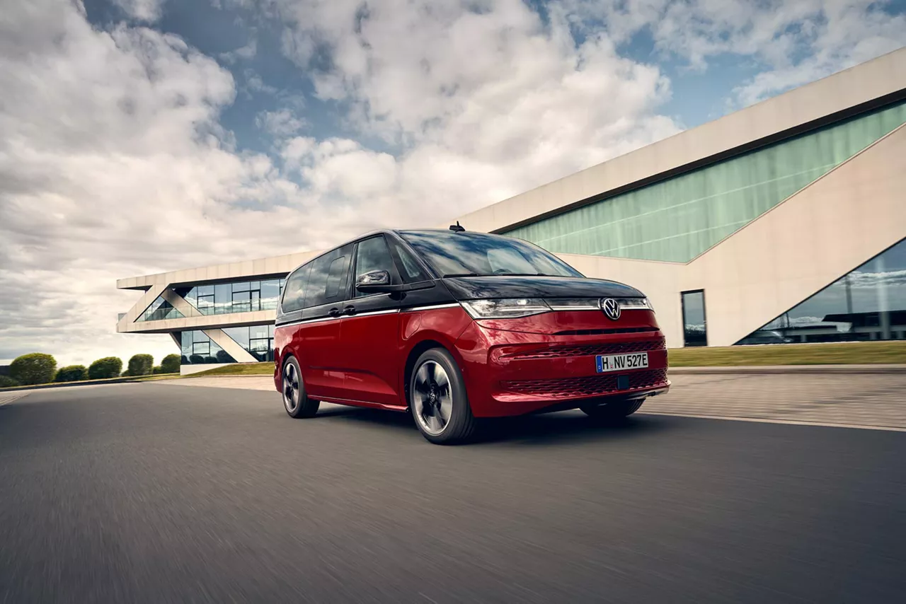 Rot schwarzer VW Multivan fährt auf einer Straße vor futuristischem Gebäude