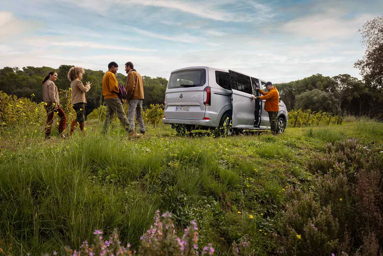 Personengruppe auf einem Wiese steigen in einen silbernen VW Caravelle ein