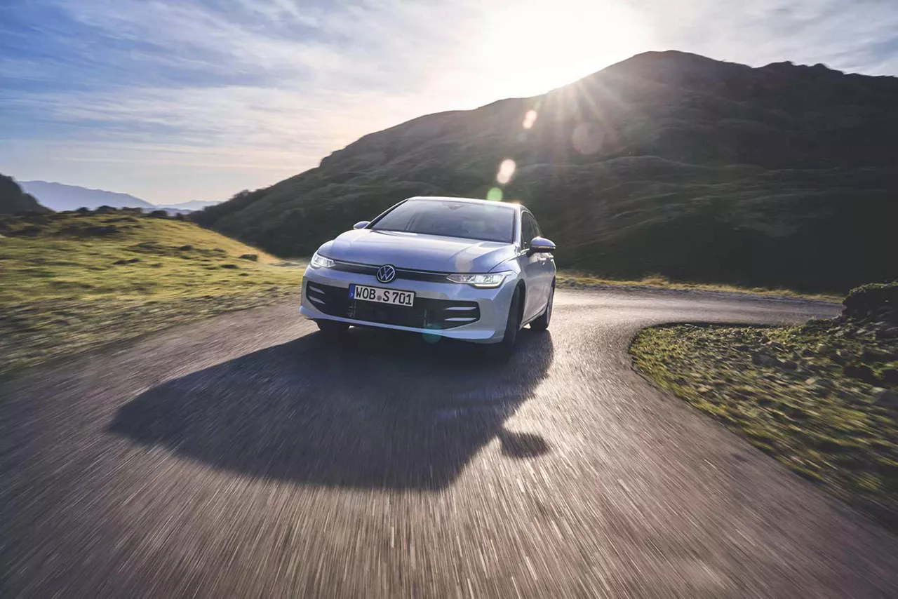 Silberner VW Golf fährt bei Sonnenschein eine Bergstrasse rauf