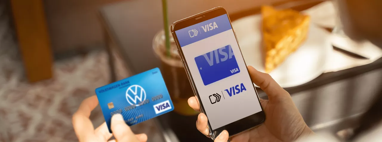 Osoba, która trzyma w jednej ręce kartę bankową, a w drugiej telefon komórkowy z wirtualny kartą Visa.