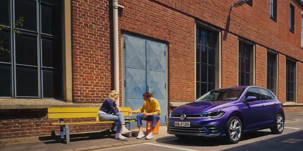 zwei-personen-sitzen-auf-bank-neben-vw-polo-violet-metallic