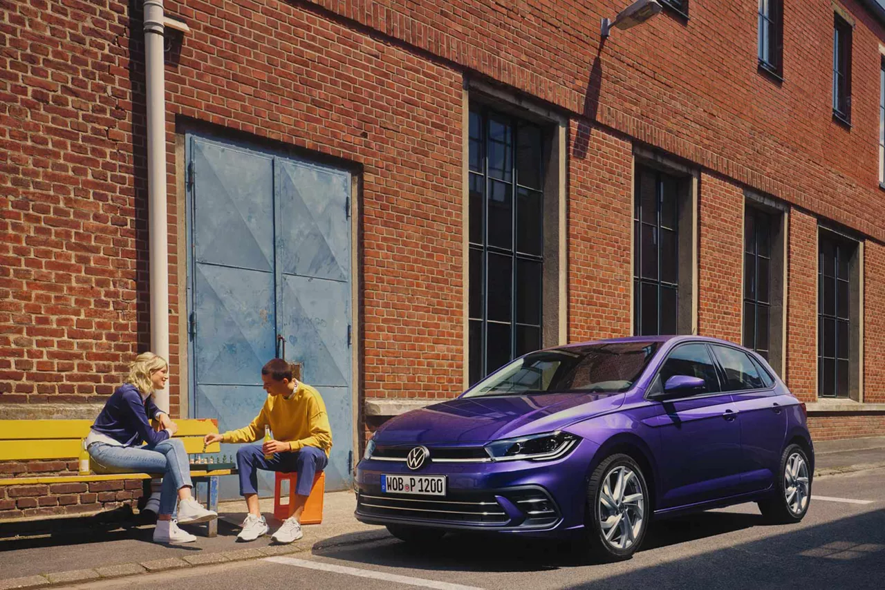 zwei-personen-sitzen-auf-bank-neben-vw-polo-violet-metallic