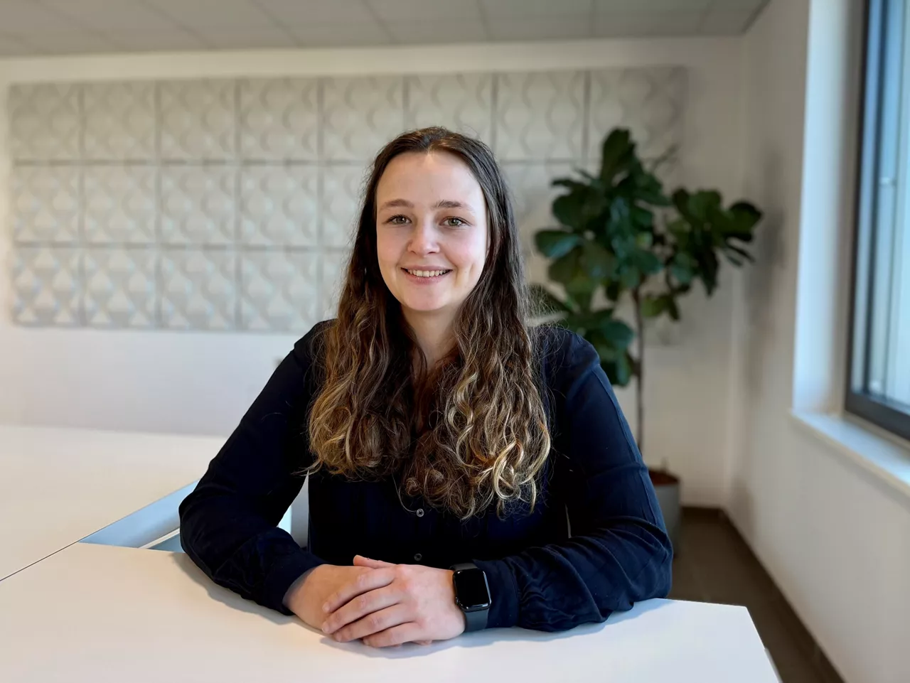 WebQuoation-Product Ownerin Vanessa Prica steht an einem Tisch. Im Hintergrund ist eine Pflanze zu sehen.