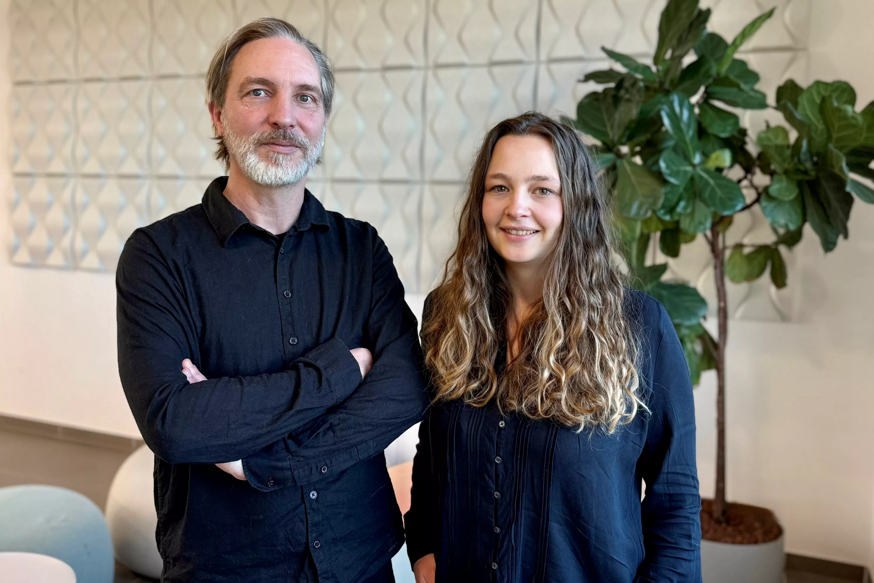 UX/UI-Experte Thomas Sander und Product Ownerin Vanessa Natalia stehen vor einer Pflanze in einem möbilierten Raum.