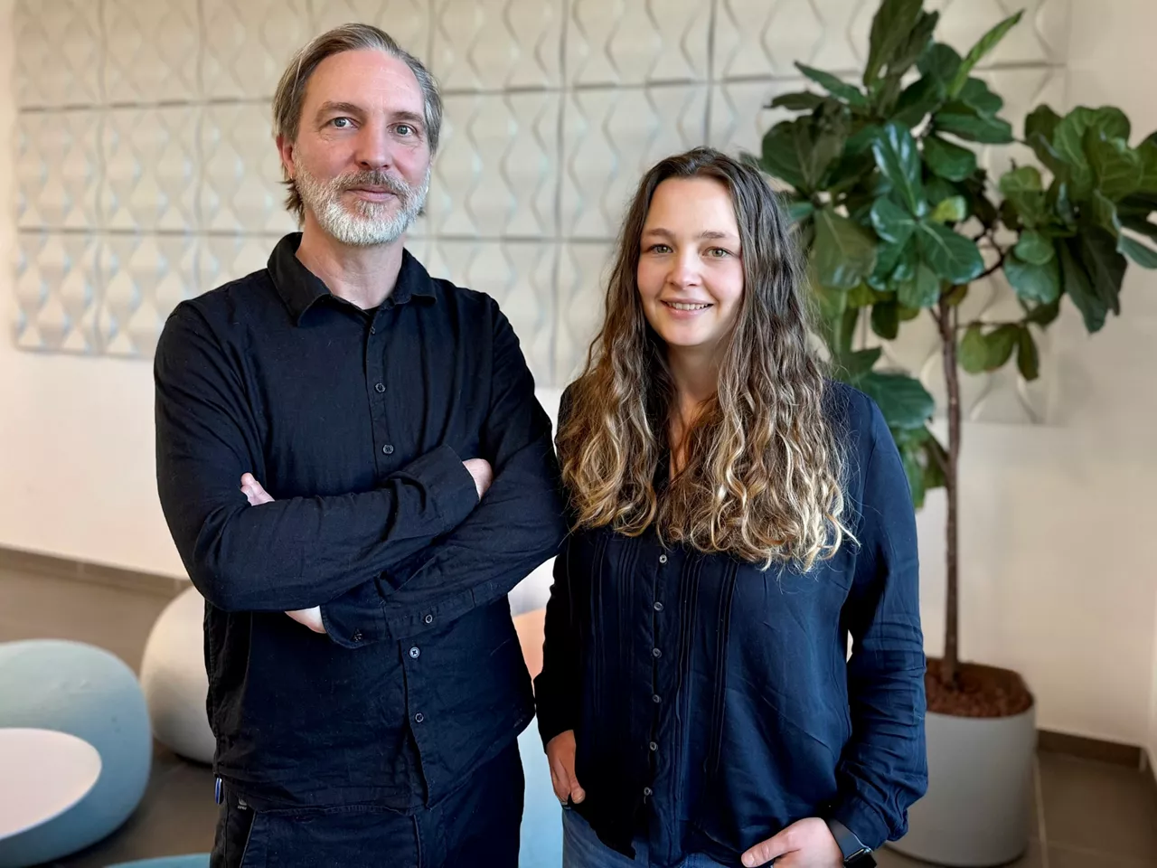 UX/UI-Experte Thomas Sander und Product Ownerin Vanessa Natalia stehen vor einer Pflanze in einem möbilierten Raum.