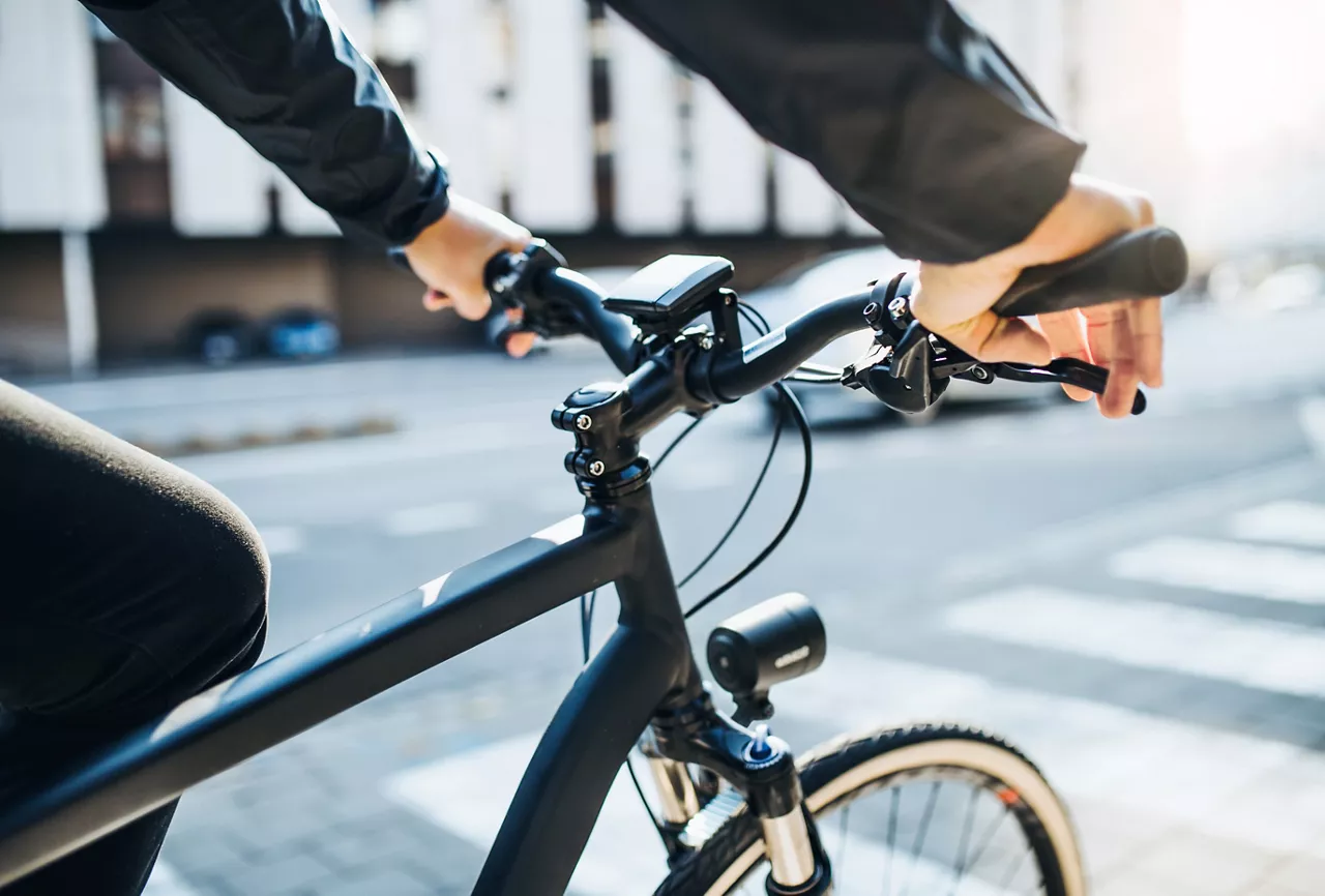 Seitliche Nahaufnahme eines Mannes mit beiden Händen am Lenker eines schwarzen Fahrrads 